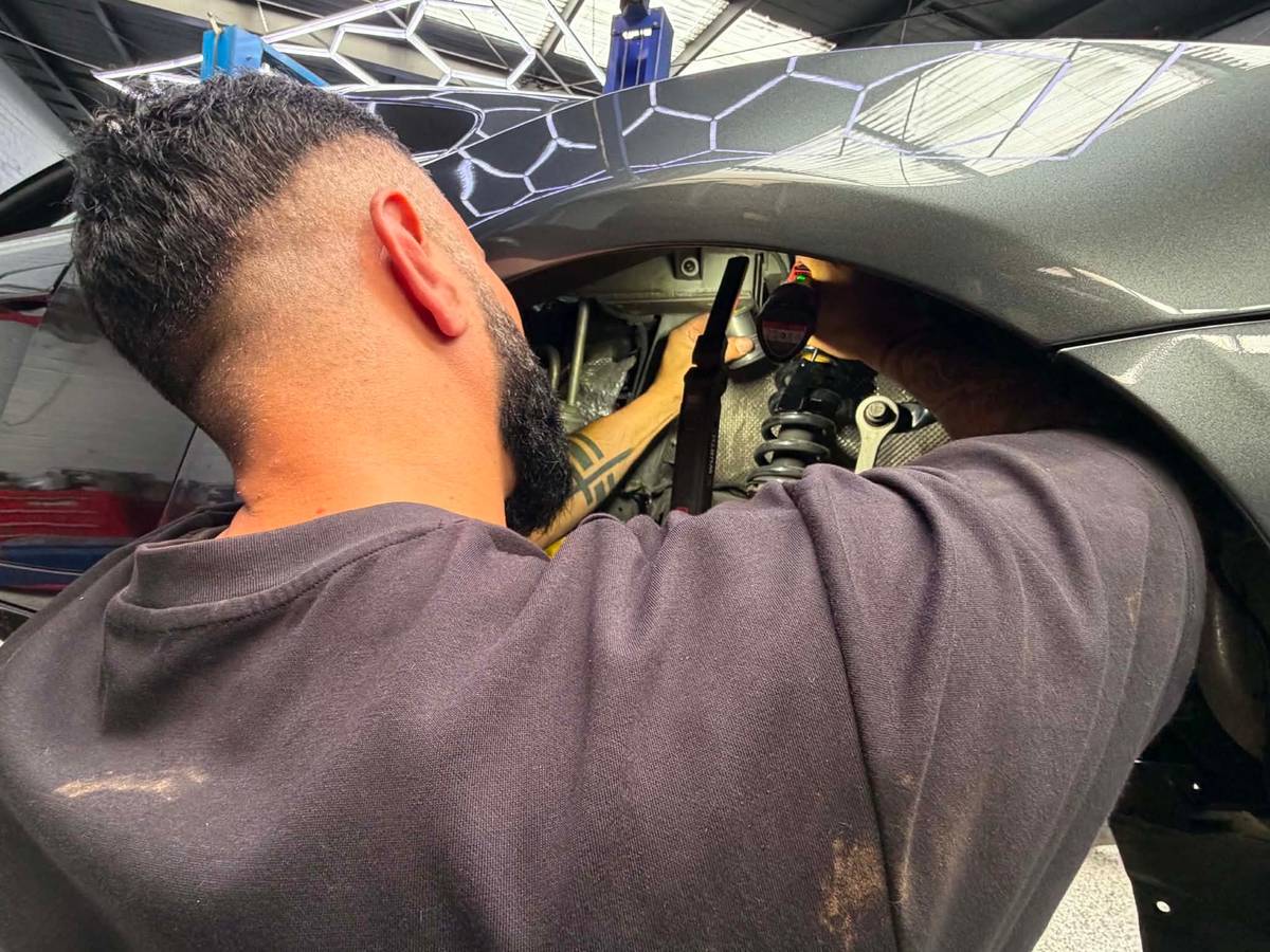 A Darwish Motors mechanic working on the front suspension of a dark European sports car